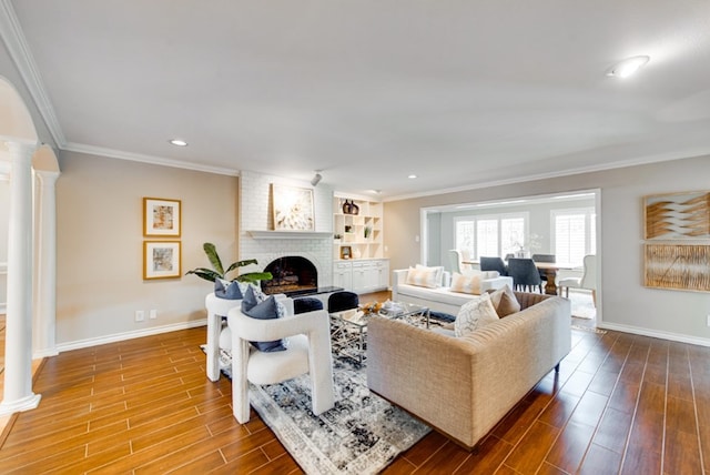 living room featuring hardwood / wood-style floors, decorative columns, a brick fireplace, and ornamental molding