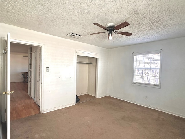 unfurnished bedroom featuring ceiling fan, a textured ceiling, a closet, and dark colored carpet