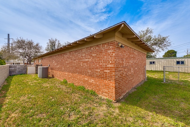 view of side of home featuring a lawn, brick siding, central AC, and fence