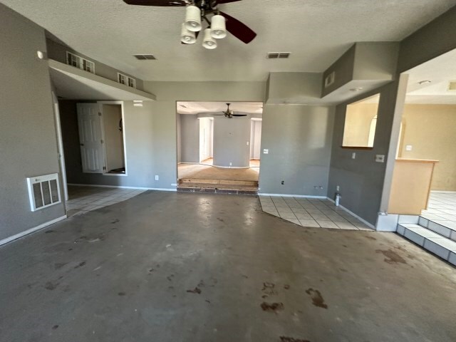 unfurnished living room featuring a textured ceiling, concrete floors, and ceiling fan