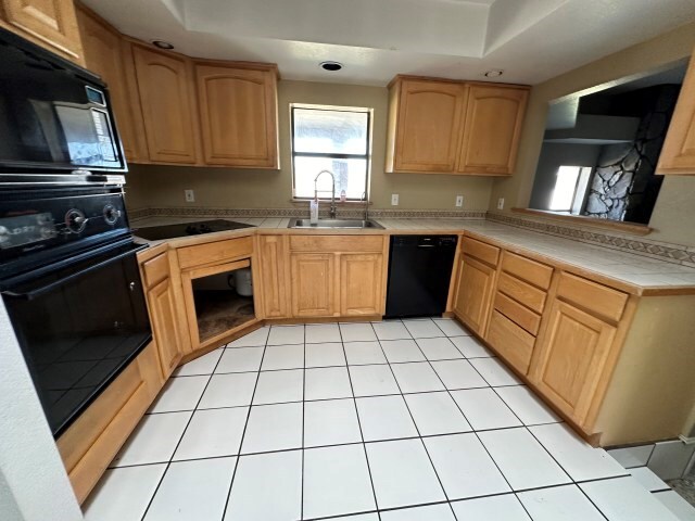 kitchen with light brown cabinets, sink, light tile patterned floors, and black appliances