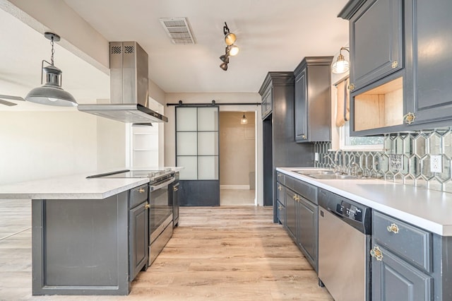 kitchen featuring stainless steel appliances, wall chimney range hood, pendant lighting, a barn door, and light hardwood / wood-style flooring