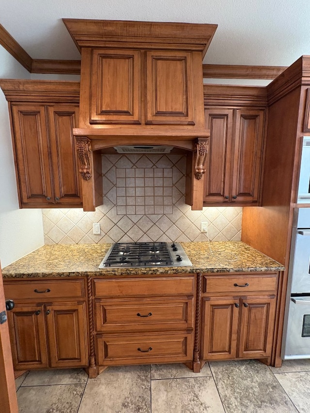 kitchen with backsplash, stainless steel gas stovetop, light stone counters, and ornamental molding