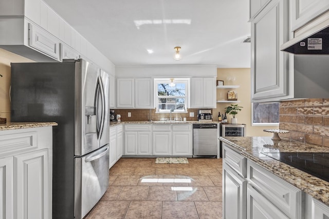 kitchen featuring light stone countertops, appliances with stainless steel finishes, white cabinets, and decorative backsplash