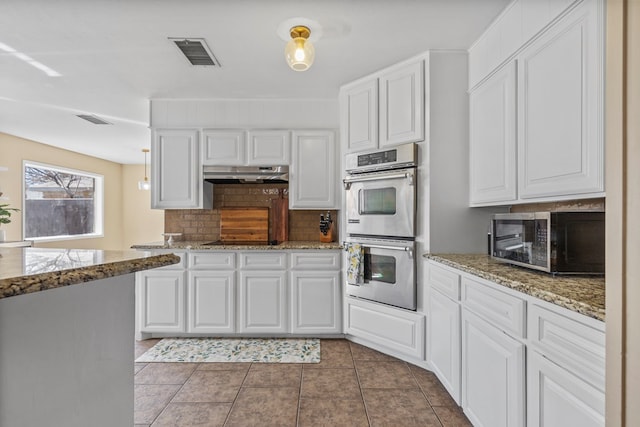 kitchen featuring dark tile patterned floors, stone counters, stainless steel appliances, decorative backsplash, and white cabinets