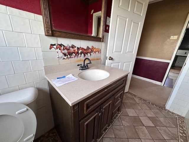 999 S County Rd 183, Snyder, TX 79549 - bathroom with toilet, vanity, tile patterned flooring, tile walls, and decorative backsplash