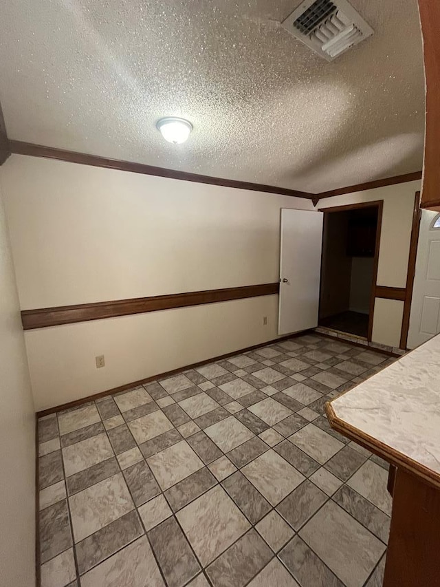 spare room with a textured ceiling, baseboards, visible vents, and crown molding