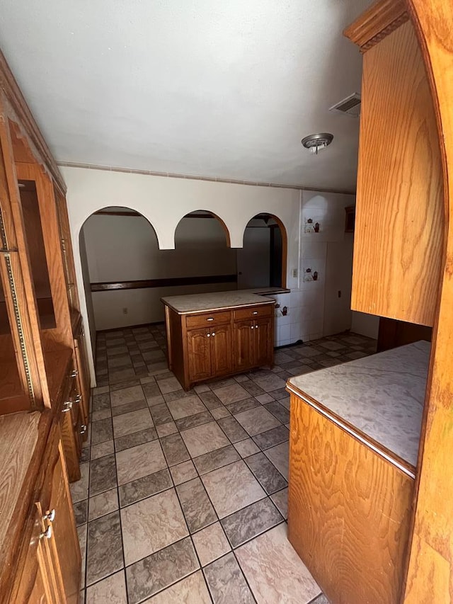 kitchen featuring visible vents, brown cabinetry, and arched walkways