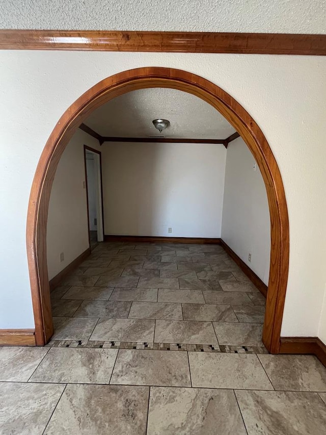 empty room featuring baseboards, a textured ceiling, arched walkways, and crown molding