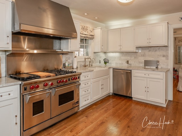 1509 Bedford Dr, Midland, TX 79701 - kitchen featuring appliances with stainless steel finishes, wall chimney range hood, crown molding, and white cabinetry