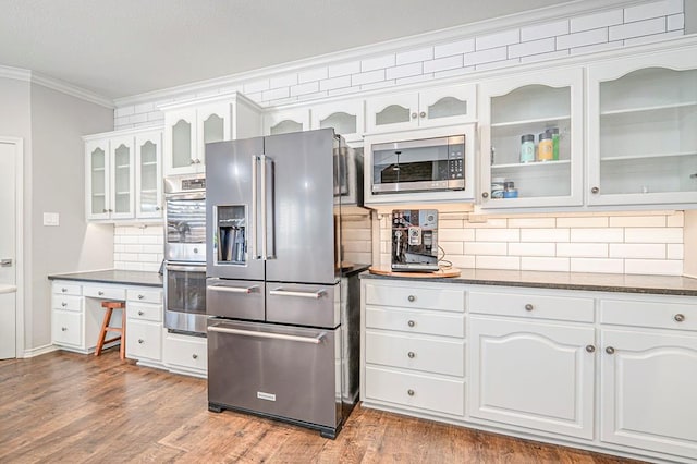 kitchen featuring white cabinets, stainless steel appliances, ornamental molding, and dark stone countertops