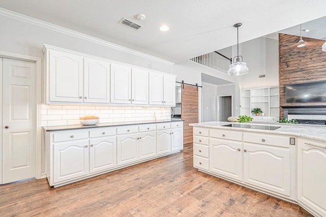 kitchen with a barn door, white cabinets, hanging light fixtures, and light wood-type flooring