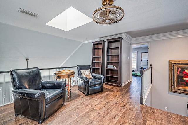 living area with wood-type flooring, a skylight, ceiling fan, and ornamental molding