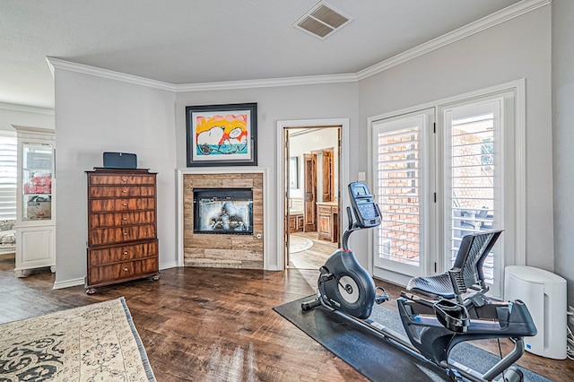 exercise area featuring a multi sided fireplace, crown molding, dark wood-type flooring, and a healthy amount of sunlight