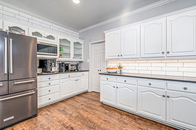 kitchen with white cabinets, crown molding, hardwood / wood-style flooring, dark stone countertops, and appliances with stainless steel finishes