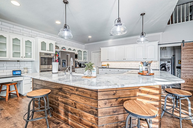 kitchen with a large island, a barn door, light stone counters, washer / clothes dryer, and white cabinets