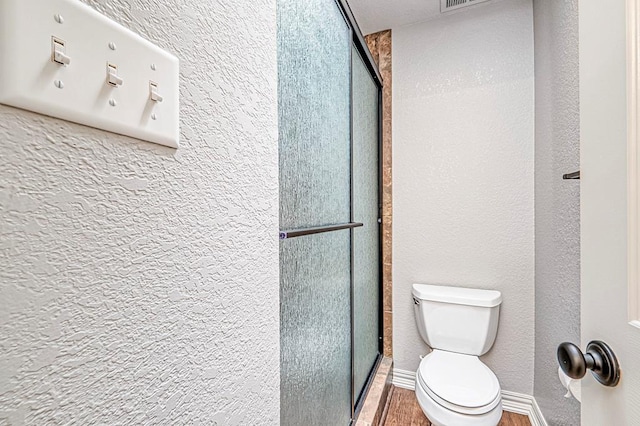 bathroom featuring hardwood / wood-style floors, toilet, and a shower with door