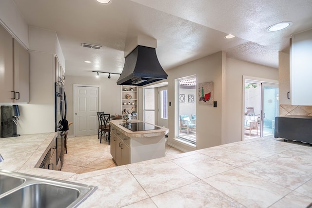 1115 Gulf Ave, Midland, TX 79705 - kitchen featuring custom range hood, black electric stovetop, a kitchen island, a textured ceiling, and light countertops