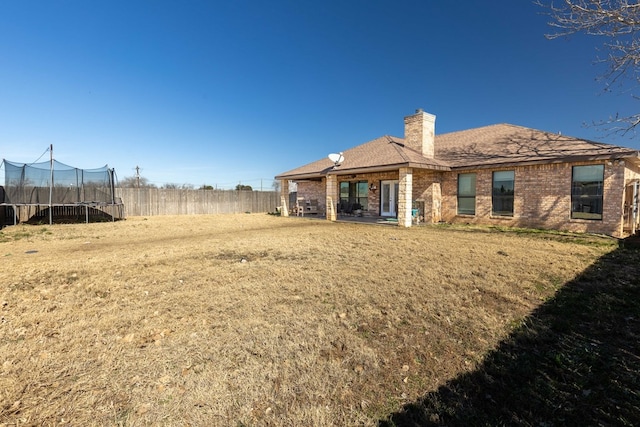 back of property with a trampoline and a yard