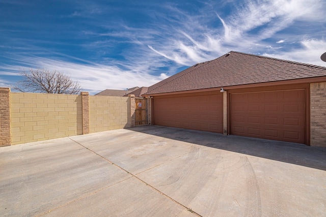 garage featuring concrete driveway and fence