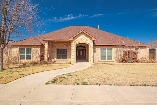 ranch-style home with a front yard, brick siding, and roof with shingles