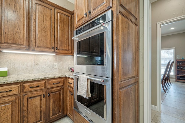 kitchen featuring double oven, light stone countertops, brown cabinetry, and tasteful backsplash