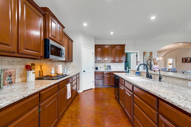kitchen with light stone counters, stainless steel appliances, backsplash, a sink, and arched walkways