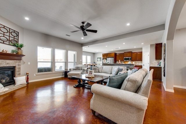 living room featuring baseboards, recessed lighting, a ceiling fan, concrete flooring, and a brick fireplace