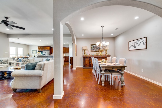dining room with ceiling fan with notable chandelier, baseboards, arched walkways, and finished concrete flooring