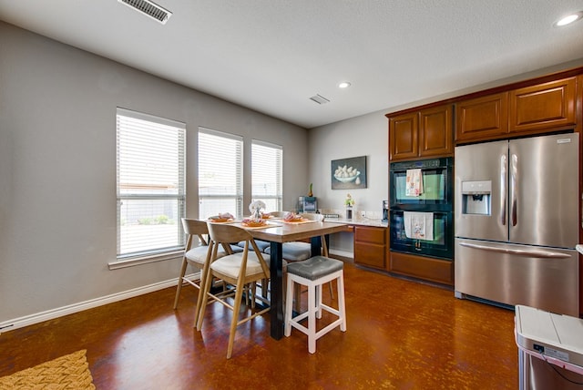 kitchen featuring stainless steel fridge, dobule oven black, baseboards, visible vents, and brown cabinets