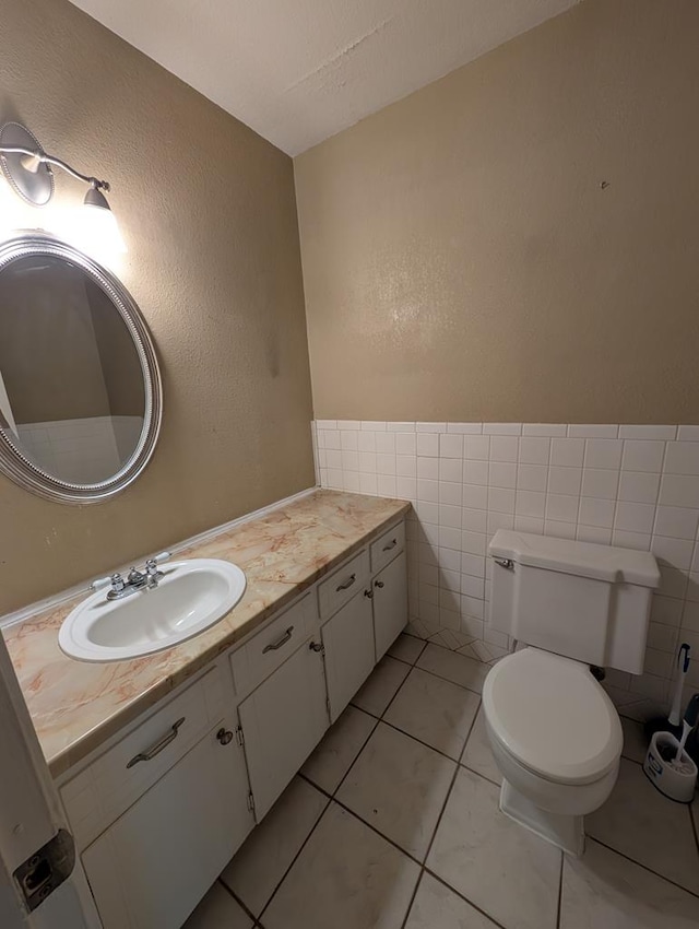 half bath with vanity, toilet, a textured wall, and tile walls