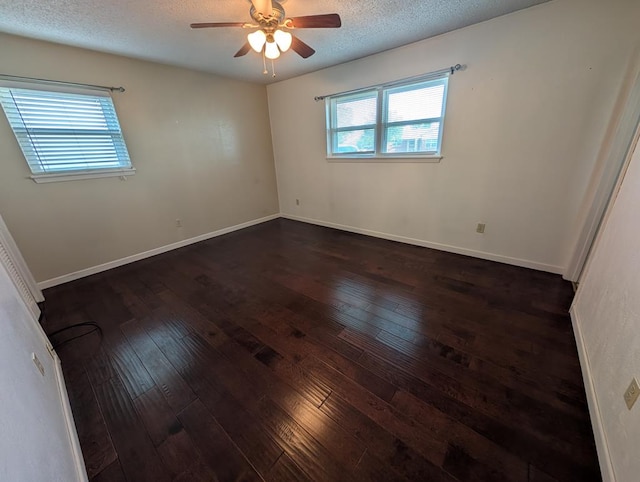 empty room with dark wood-style floors, healthy amount of natural light, a ceiling fan, a textured ceiling, and baseboards