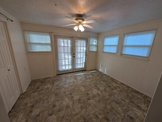 empty room with a ceiling fan, french doors, a textured ceiling, baseboards, and crown molding