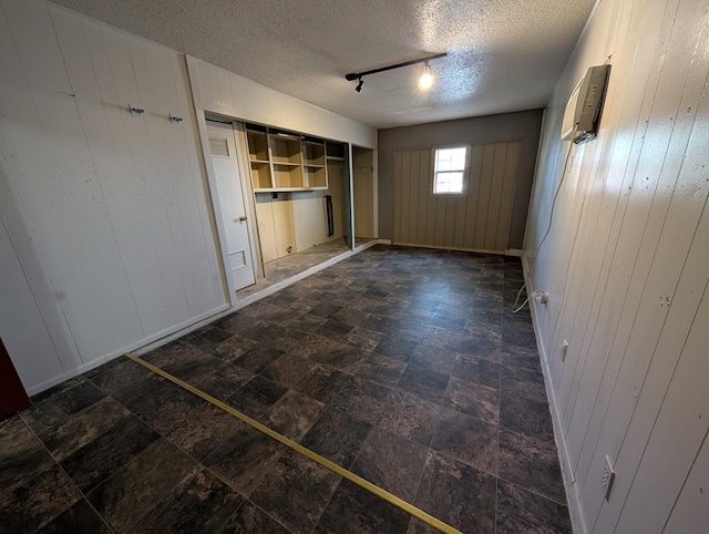 unfurnished bedroom featuring rail lighting, a textured ceiling, and wood walls