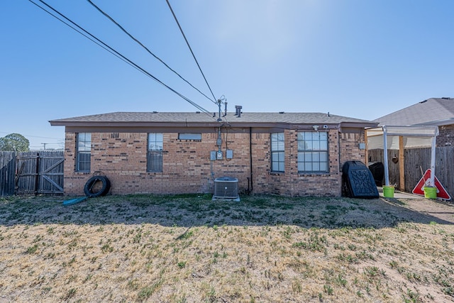 rear view of house with cooling unit, brick siding, a yard, and fence