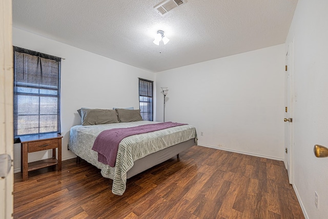 bedroom with visible vents, baseboards, a textured ceiling, and wood finished floors