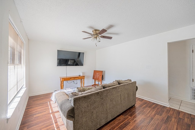 living area featuring a textured ceiling, wood finished floors, baseboards, and ceiling fan