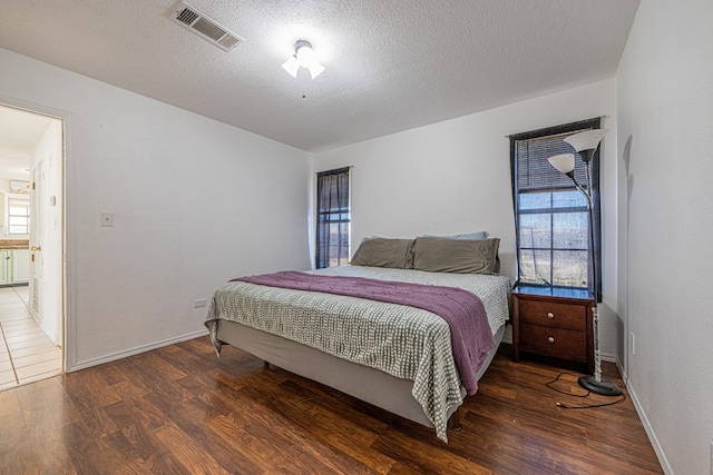 bedroom with visible vents, a textured ceiling, baseboards, and wood finished floors