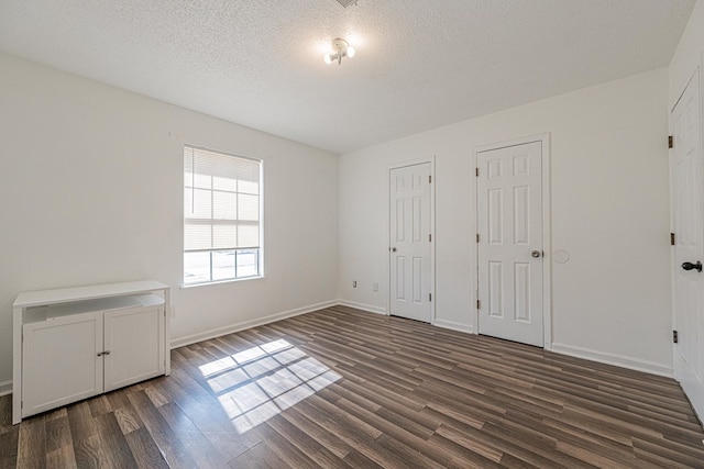 unfurnished bedroom with baseboards, dark wood-type flooring, multiple closets, and a textured ceiling