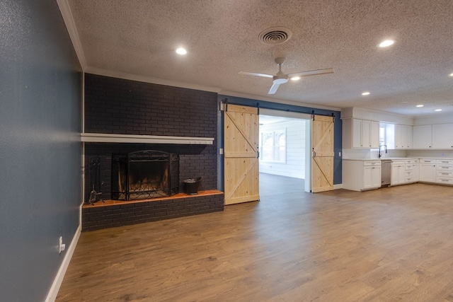 709 21st St, Lamesa, TX 79331 - unfurnished living room with a textured ceiling, a barn door, crown molding, wood finished floors, and a brick fireplace