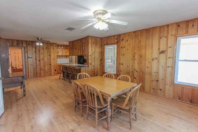 dining area featuring ceiling fan, light wood-type flooring, a textured ceiling, and wooden walls