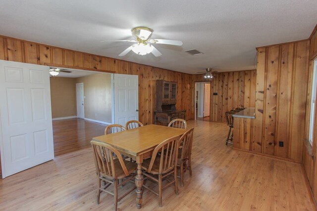 dining area with wood walls, light wood-type flooring, and a textured ceiling