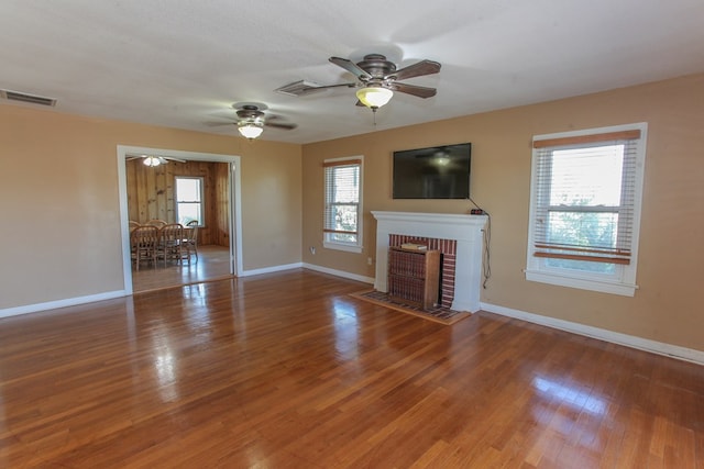 unfurnished living room with hardwood / wood-style floors, a wealth of natural light, and a brick fireplace