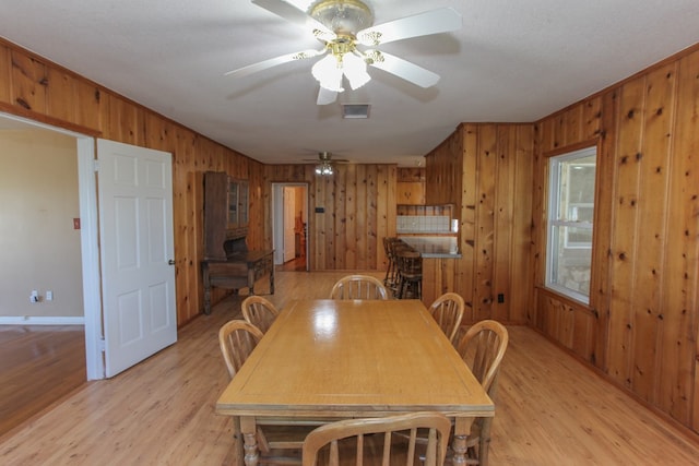 dining space featuring wood walls, ceiling fan, light hardwood / wood-style floors, and a textured ceiling