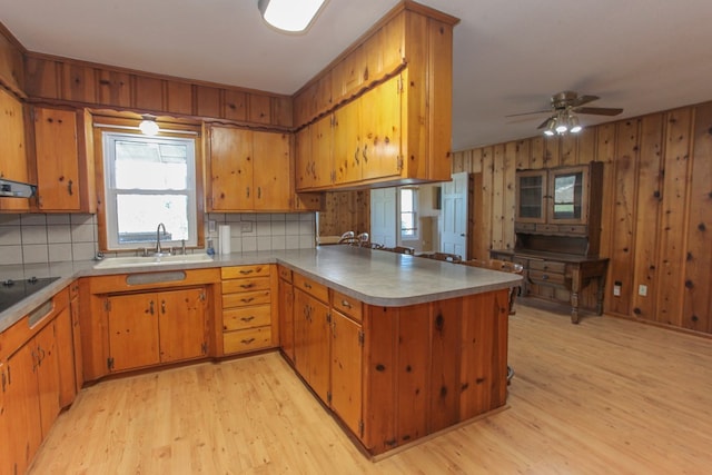 kitchen featuring sink, wooden walls, decorative backsplash, light wood-type flooring, and kitchen peninsula