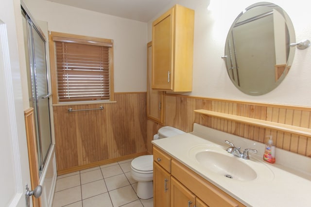 full bathroom with tile patterned floors, wood walls, toilet, shower / bath combination with glass door, and vanity