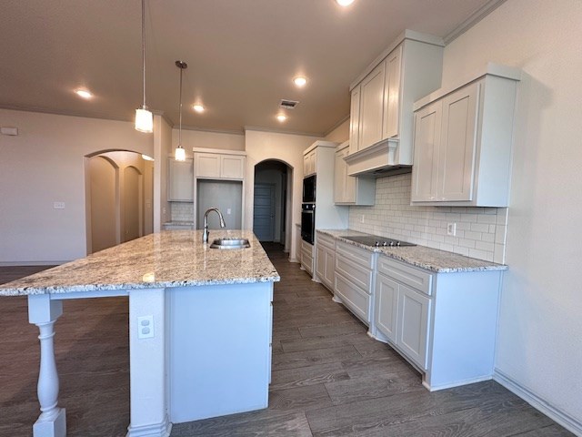 3210 Fordham Ave, Big Spring, TX 79720 - kitchen with arched walkways, black electric stovetop, custom exhaust hood, stainless steel oven, and decorative backsplash