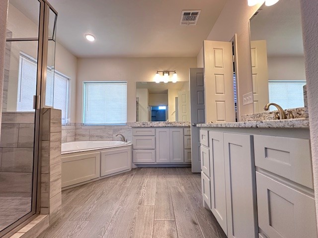 3210 Fordham Ave, Big Spring, TX 79720 - bathroom with wood finished floors, a shower stall, two vanities, and a garden tub