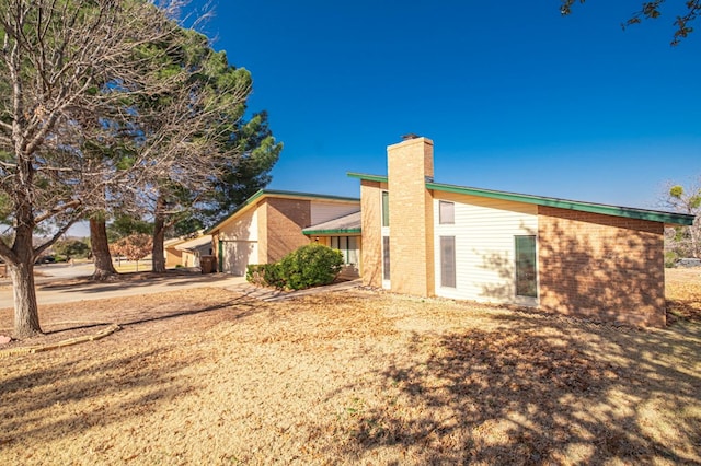 view of property exterior featuring brick siding, driveway, and a chimney