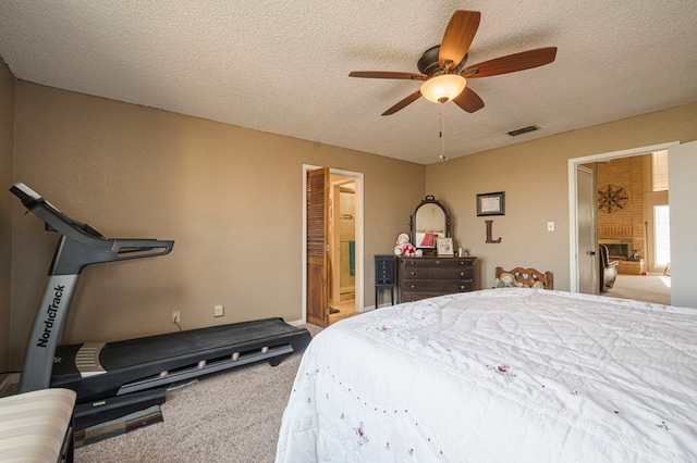 bedroom featuring carpet, visible vents, a brick fireplace, ceiling fan, and a textured ceiling